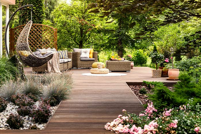 Große WPC-Terrasse mit Gartenmöbeln inmitten von Grün, umrandet von Blumenbeeten